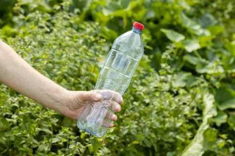 Hand holding crumpled empty plastic bottle in the park Stock Photos