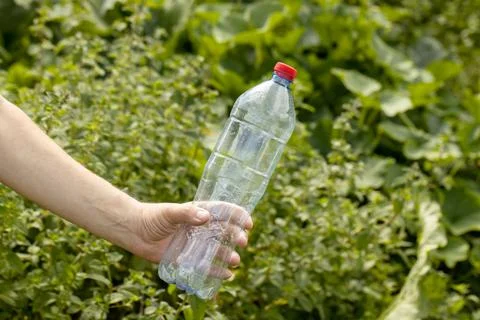 Hand holding crumpled empty plastic bottle in the park Stock Photos