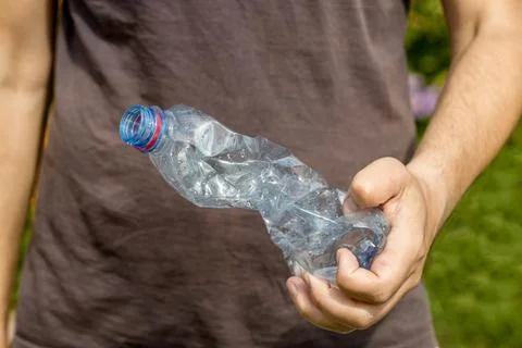 Hand holding crumpled empty plastic bottle in the park Stock Photos