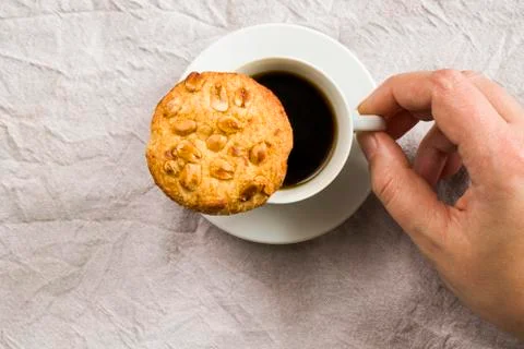 A hand holding a cup of black espresso coffee and cooky on the white cloth ba Stock Photos