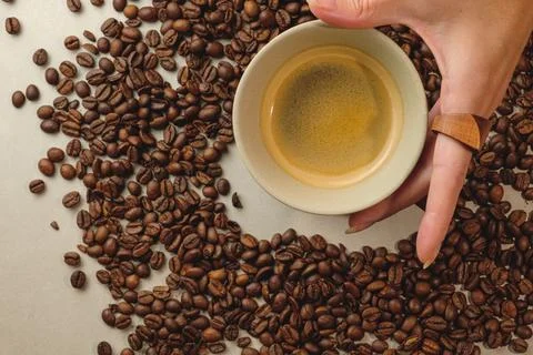 Hand holding a cup of coffee surrounded by fresh coffee beans Stock Photos