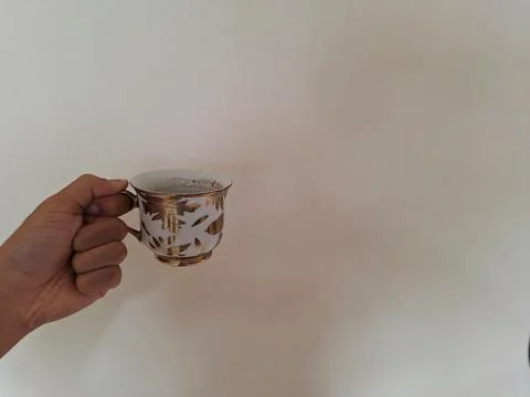 A hand holding a cup with a gold pattern filled with coffee. Stock Photos