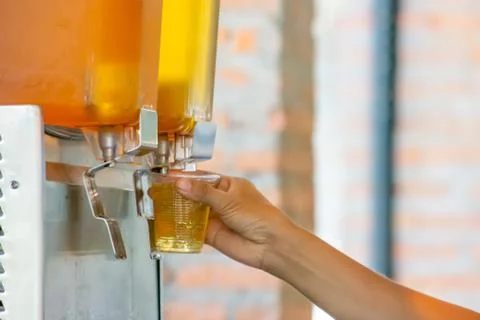 The hand holding the cup plastic flush tea from Juice Dispensor. Stock Photos