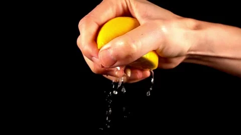 Hand holding a cut slice of lemon and squeeze the fresh juice with black ba.. Stock Footage 265839458