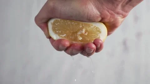Hand holding a cut slice of lemon and squeeze the fresh juice with white Stock-Footage 336588797