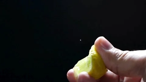 Hand holding a cut slice of lemon and squeeze the fresh juice with black Stock-Footage 336588907