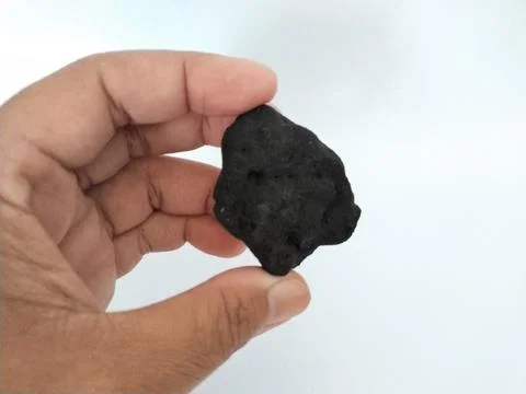 Hand holding a dark, irregular shaped rock against a white background Stock Photos