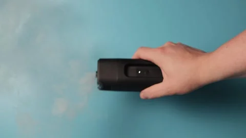 Hand holding a device emitting white smoke against a blue background Stock Footage 340265885