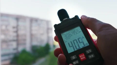 Hand Holding Digital Decibel Meter Measuring Noise Level Near City Building Stock Footage 338100759