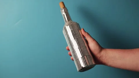 Hand holding a disco ball bottle with cork on blue background Stock Footage 340266895