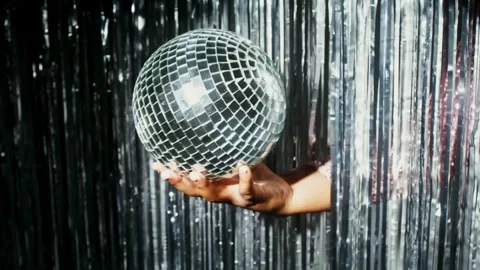 Hand holding disco ball in front of foil fringe silver curtains background. Stock Footage 265757425