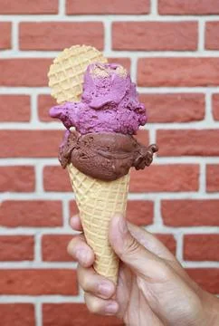 Hand holding a double scoop of raspberry yogurt and dark chocolate gelato cone Stock Photos