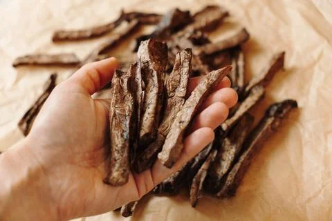 Hand holding dried beef lung strips over natural dog treats. Healthy single.. Stock Photos