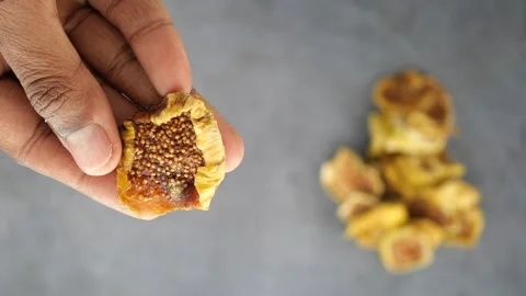 Hand holding dried fig on grey surface with more figs nearby Stock Footage 333444349