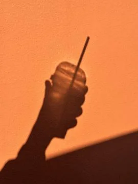 Hand holding a drink casting shadow on orange wall Stock Photos