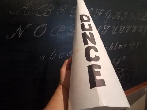 Hand holding dunce cap hat in front of chalkboard Stock Photos