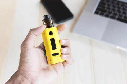Hand holding e-cigarette over work table Stock Photos