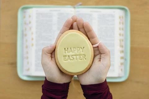 Hand holding Easter cookie with greeting over open Bible at home. Foto stock