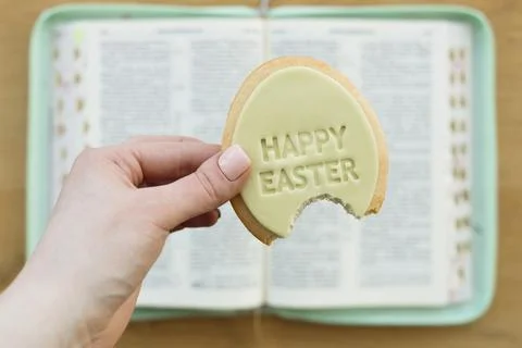 Hand holding Easter egg shaped cookie with Happy Easter text over open Bible. Stock Photos