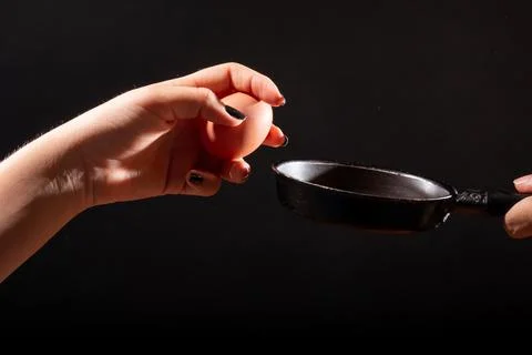 Hand holding egg in front of frying pan. isolated on black background. Hand Stock Photos