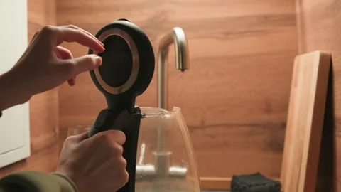 Hand holding electric kettle with lid open above glass coffee carafe beside Vidéo 345663628