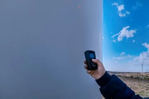 Hand holding electronic device inspecting wind turbine for renewable energy Stock Photos