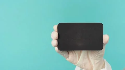 Hand holding empty blank black card.Hand with ppe suit, latex glove on green  Stock Photos