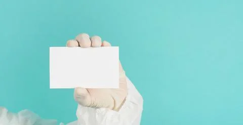 Hand holding empty blank white card.Hand with ppe suit, latex glove on green  Stock Photos