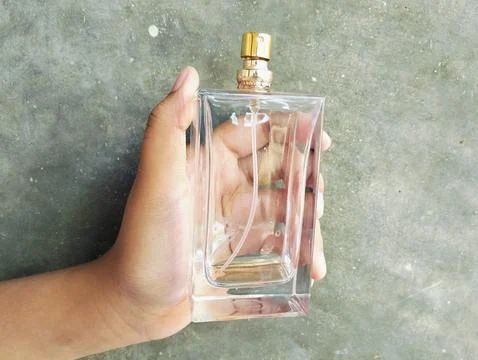 Hand Holding an Empty Perfume Bottle on Concrete Wall Background Photos