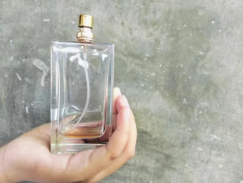 Hand Holding an Empty Perfume Bottle on Concrete Wall Background Fotos Stock