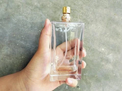 Hand Holding an Empty Perfume Bottle on Concrete Wall Background Photos