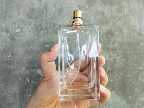 Hand Holding an Empty Perfume Bottle on Concrete Wall Background Photos