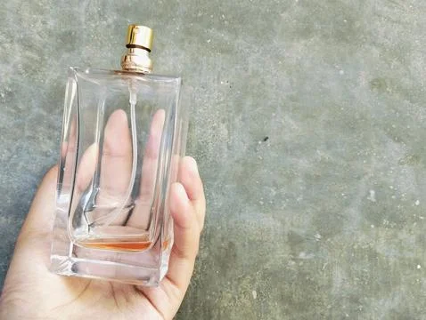 Hand Holding an Empty Perfume Bottle on Concrete Wall Background Fotos Stock
