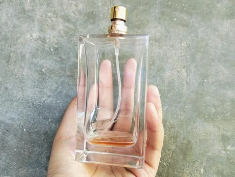 Hand Holding an Empty Perfume Bottle on Concrete Wall Background Photos