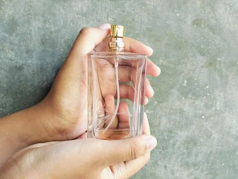Hand Holding an Empty Perfume Bottle on Concrete Wall Background Photos