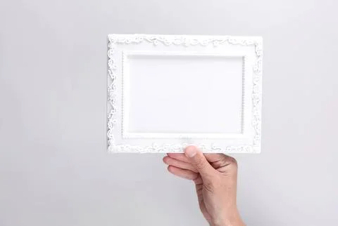 Hand holding empty white decorative picture frame on gray background Photos
