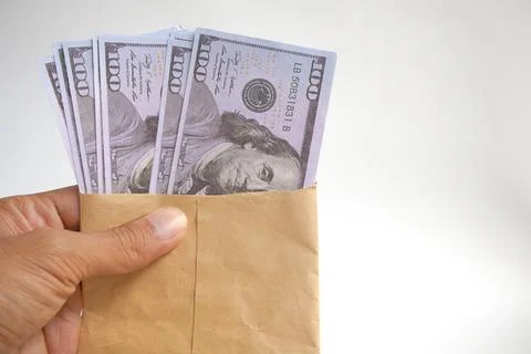 Hand holding an envelope containing 100 dollar bills on a white background Stock Photos