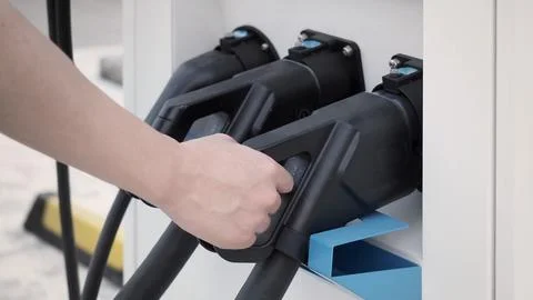 Hand holding EV charging plug in front of camera with blurred background Stock Photos