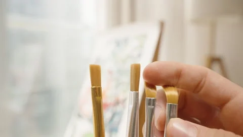 Hand Holding Five Different Small Paintbrushes in Front of Bright Window and Stock Footage 306453315