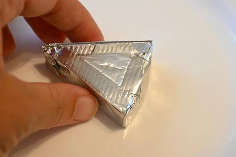 Hand holding a foil-wrapped processed cheese wedge Stock-Fotos