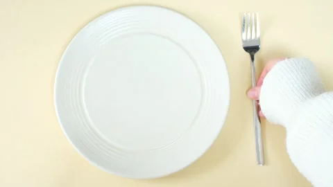 Hand holding a fork next to an empty plate on brown background close-up top view Stock Footage 329599882