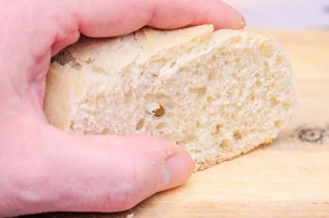 Hand holding a fresh piece of bread on a wooden cutting board Stock Photos