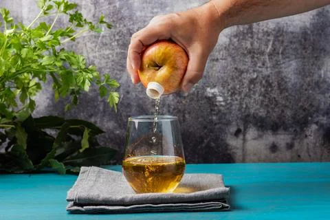 Hand holding a fruit, apple, which has a spout through which it pours the j.. Stock Photos
