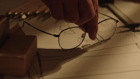 Hand Holding Glasses Over Architectural Sketches on Desk Stock-Footage 337415124