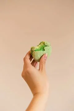 Hand holding green cookie with bite taken out on beige background Stock Photos