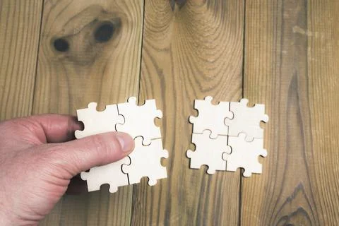 Hand holding a group of four interconnected puzzle pieces to connect them to Foto stock