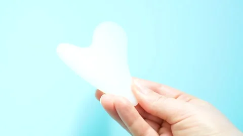A hand holding gua sha face massager on blue background. Stock Footage 329273573