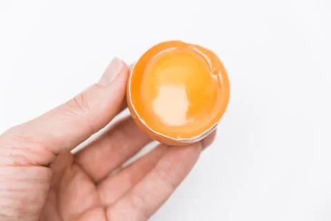 A hand holding half broken egg with yellow yolk in a shell against white Stock Photos