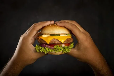 Hand holding hamburger on dark background. Stock Photos