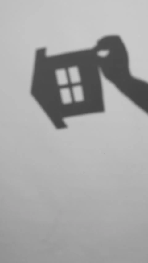 Hand Holding a House Cutout Shadow Moves and Rotates on a Light Wall Stock Footage 327963156